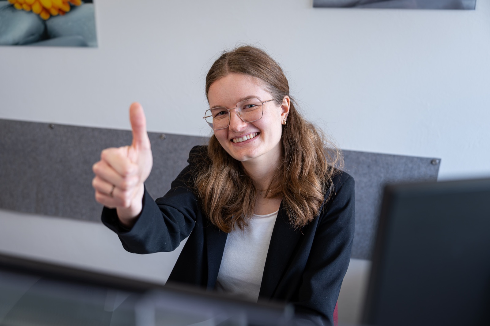 Junge Mitarbeiterin am Arbeitsplatz mit positivem Gestus